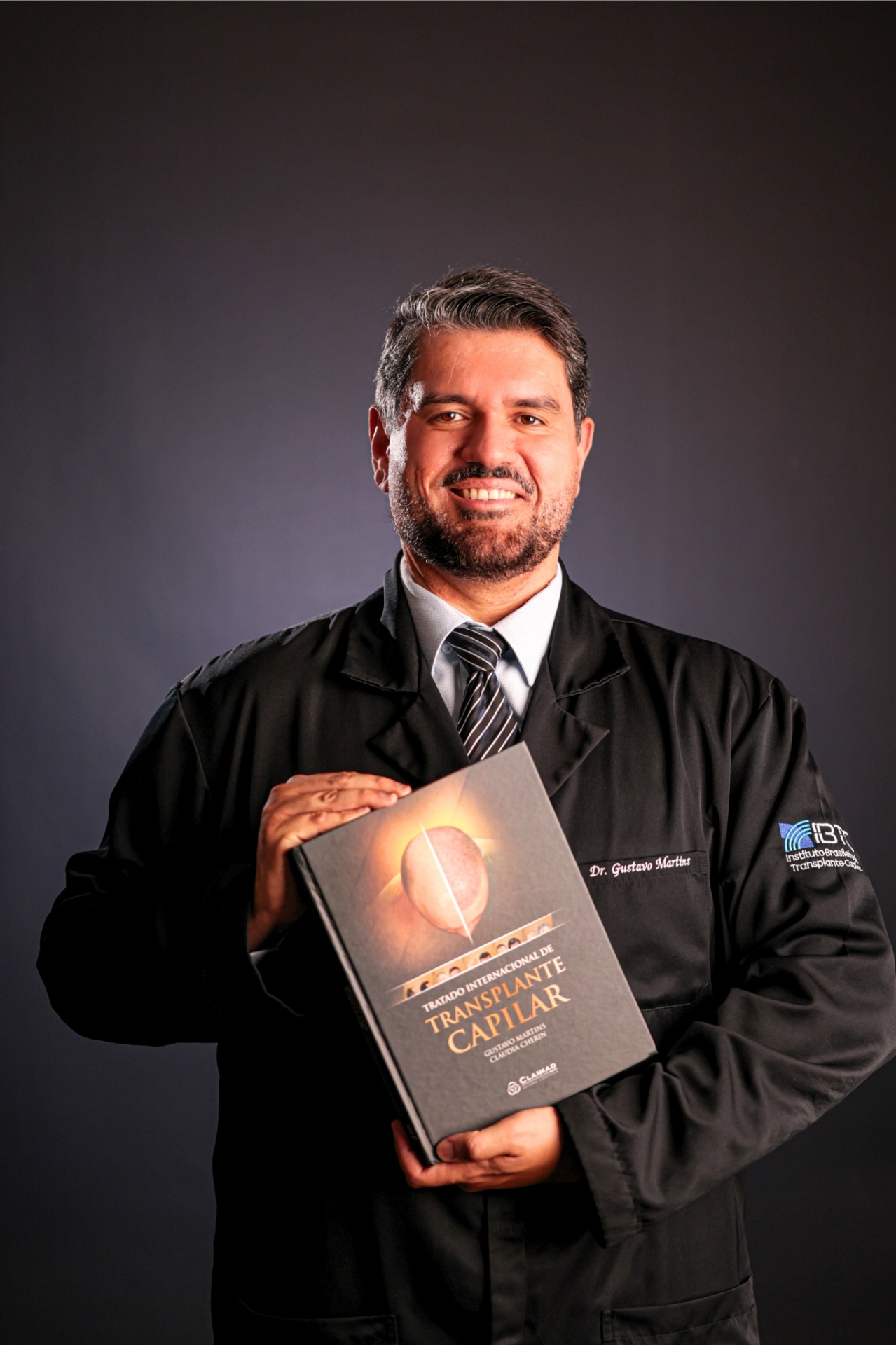 Dr. Gustavo Martins segurando o Tratado Internacional de Transplante Capilar